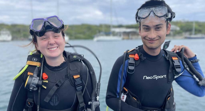 Two people in scuba gear sit above water and smile for the photo